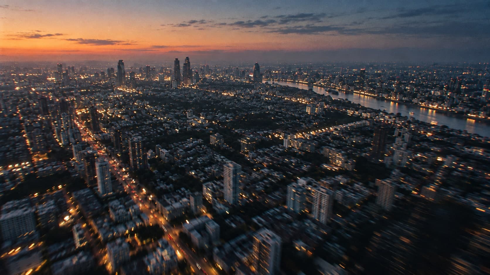 A city at dusk from above, streets lit and blurred with motion
